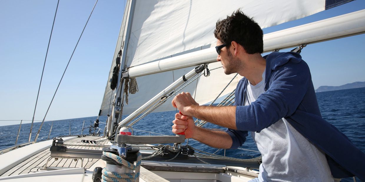 A man adjusting the sail on a sailboat under a clear blue sky.
