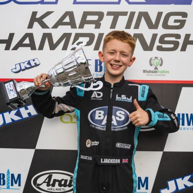 Young karting champion holding trophy and giving thumbs up.