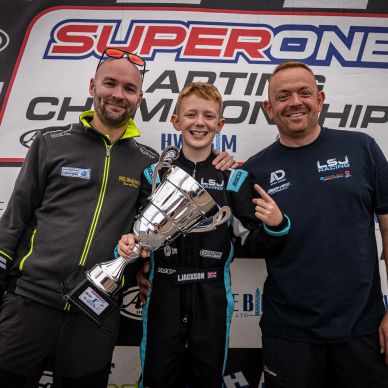 Young karting champion with two men and a trophy.