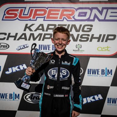 Young karting champion holding a trophy and smiling.
