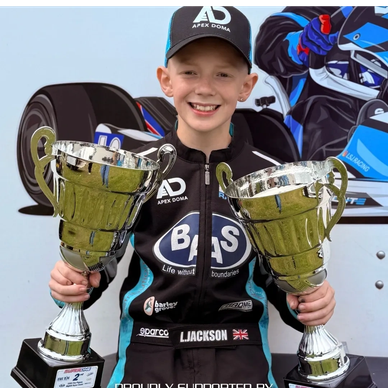 Young racer holding two trophies and smiling.