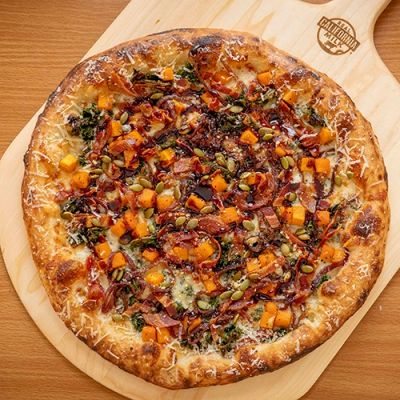 A freshly baked pizza topped with vibrant vegetables and herbs on a wooden board.