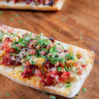 Open-faced sandwich with herbs, bacon, and cheese on a wooden board.