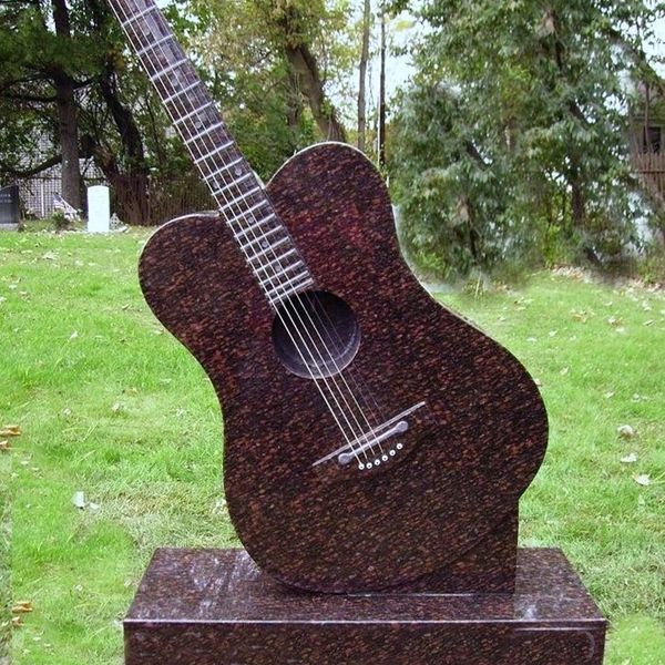 A guitar-shaped tombstone in a grassy cemetery.