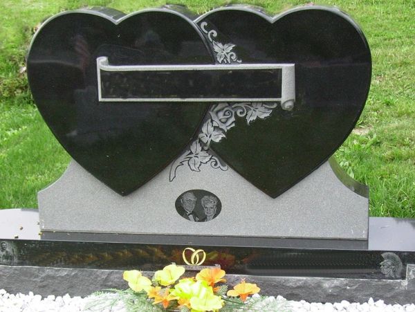 Double heart-shaped gravestone with floral engravings and a photo of an elderly couple.