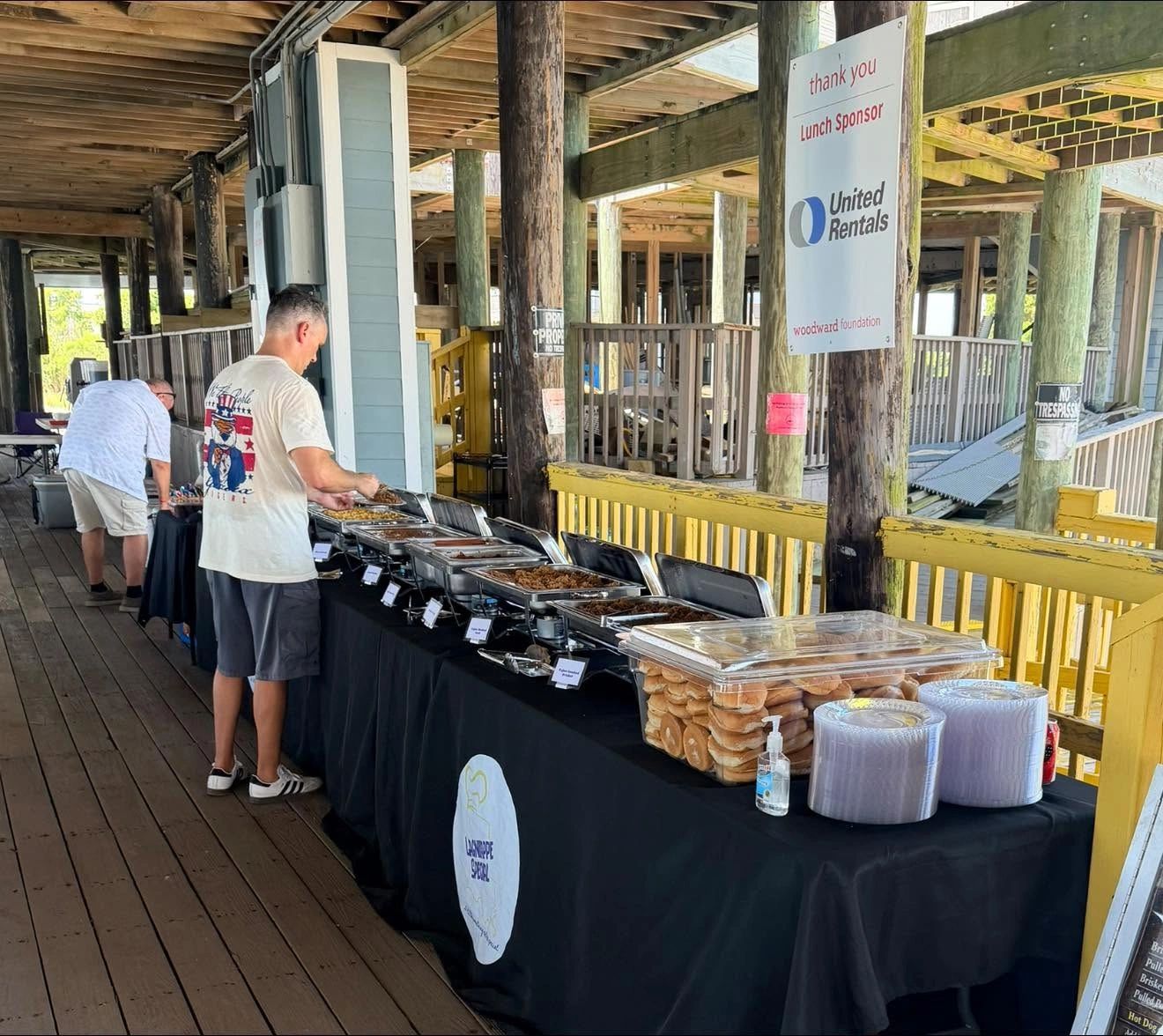 People serving themselves from a buffet at an outdoor wooden pavilion.