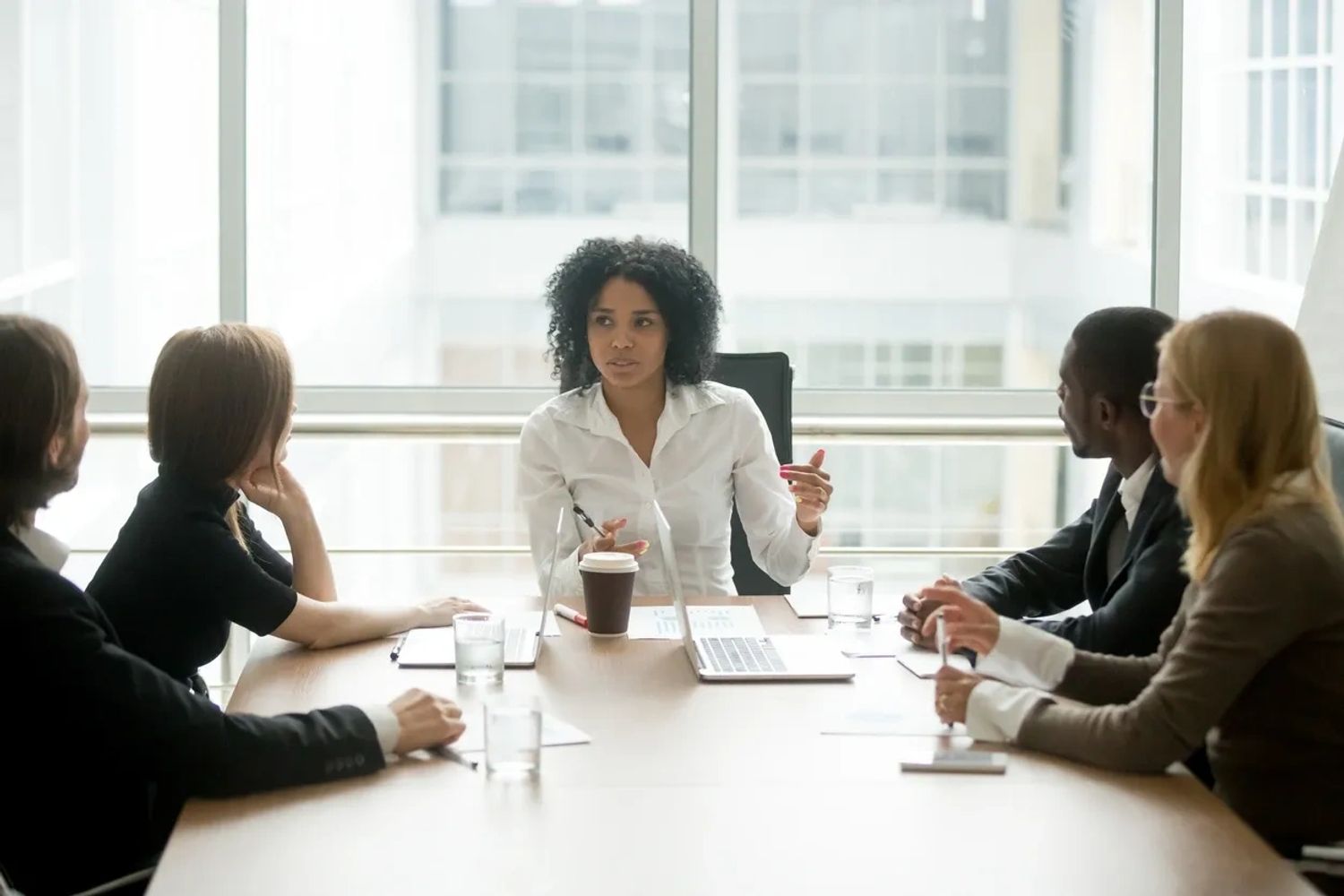 A woman leads a business meeting with four attentive colleagues around a conference table.