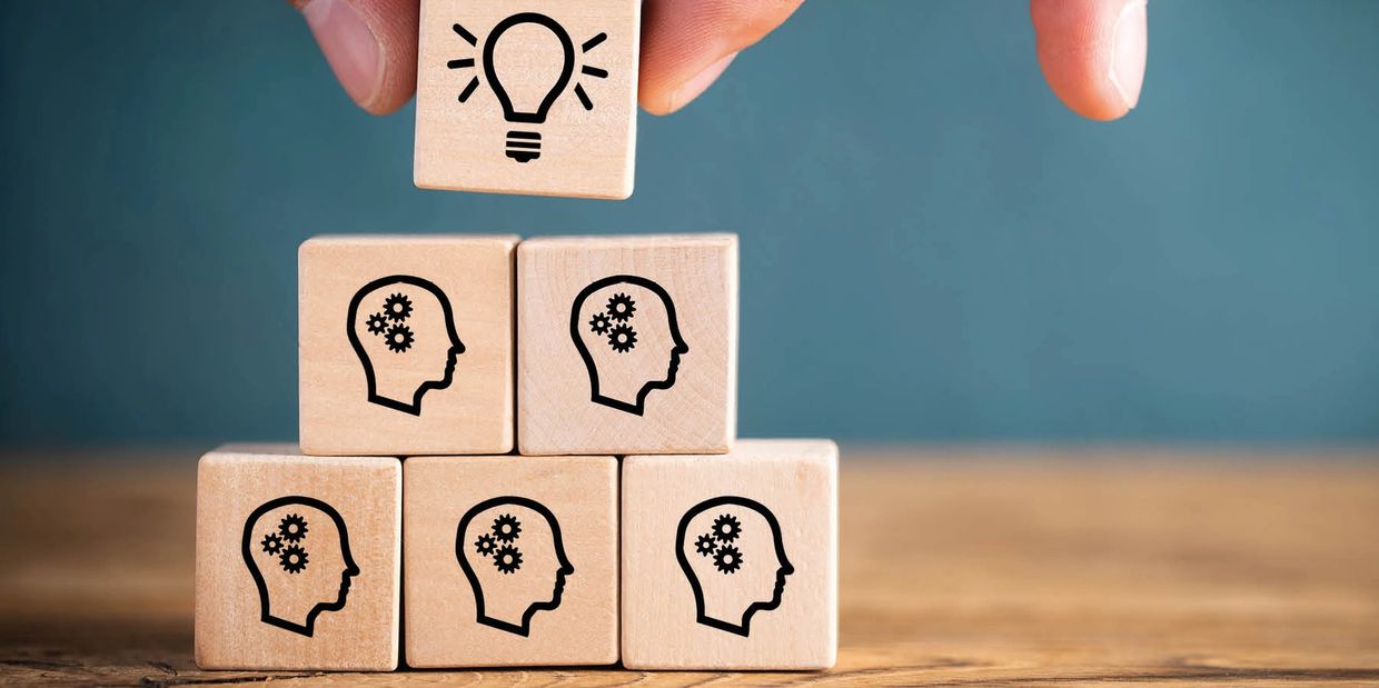 Wooden blocks with human head icons and a lightbulb symbolizing ideas and innovation.