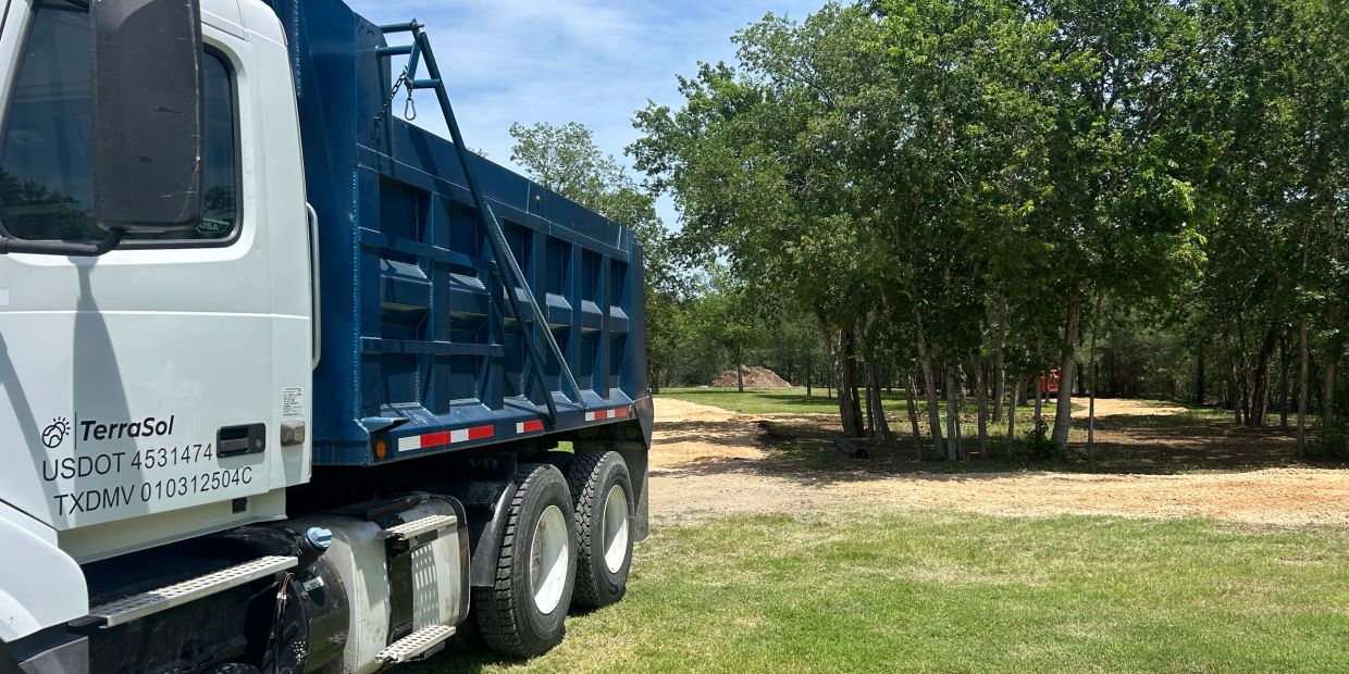 A TerraSol dump truck parked next to a dirt path surrounded by trees.