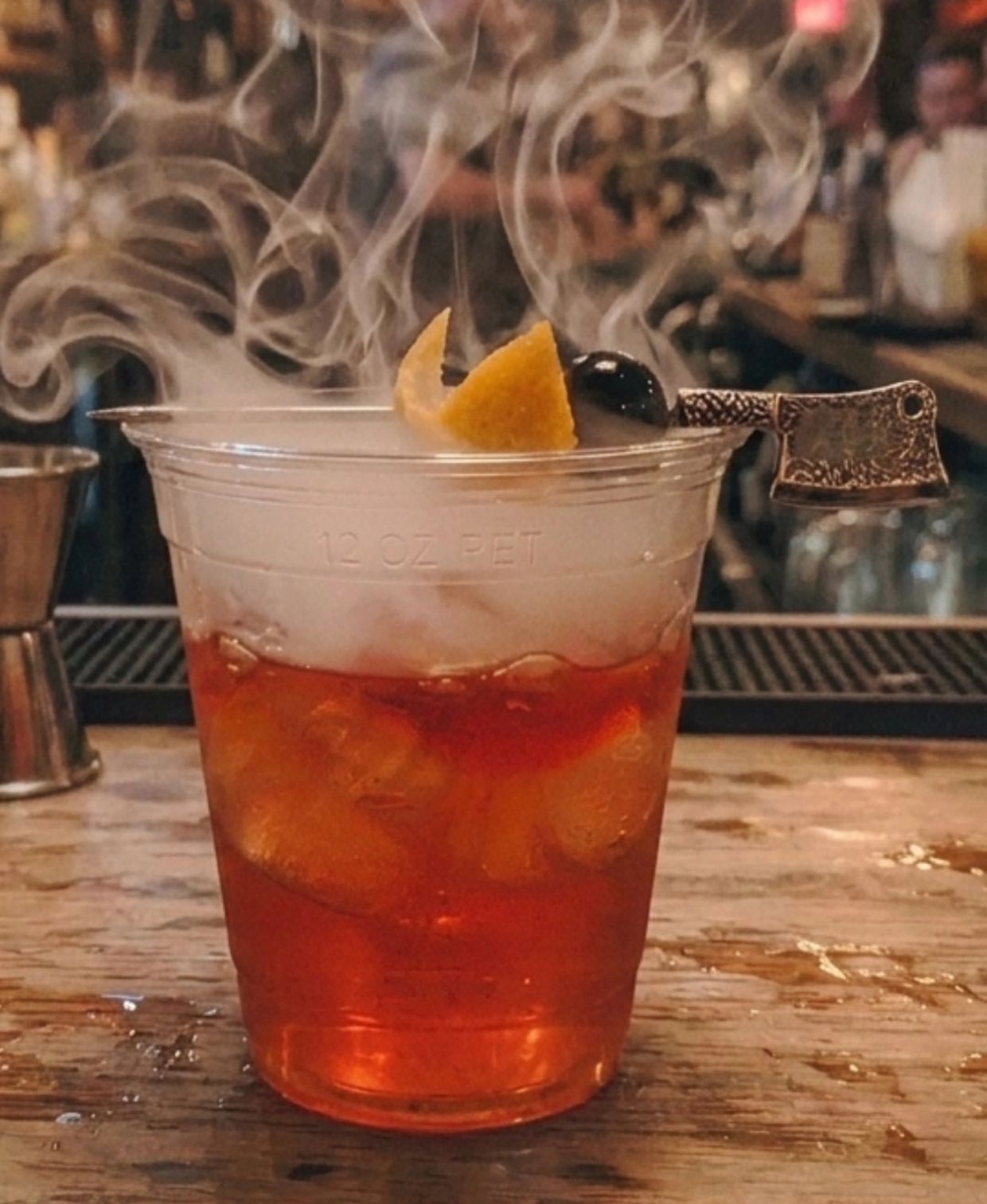 Smoky cocktail in a clear plastic cup with a decorative skewer.