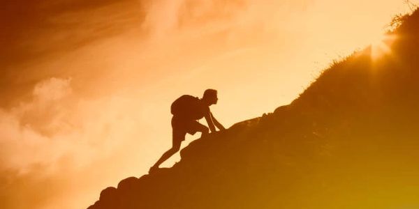 Silhouette of a person climbing a steep hill at sunset.