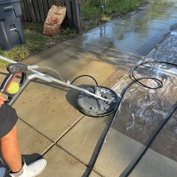 Person pressure washing a concrete driveway on a sunny day.