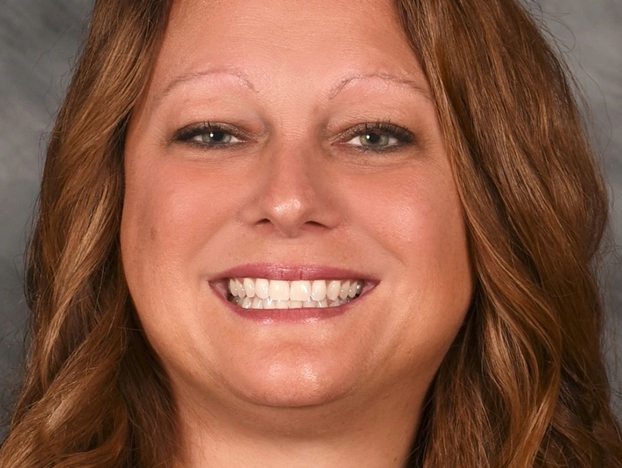 Smiling woman with wavy brown hair against a neutral background.