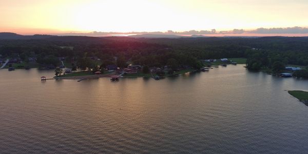 A peaceful lakeside sunset over a wooded shoreline with homes.