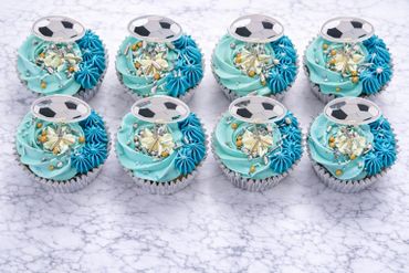 Eight blue soccer-themed cupcakes with soccer ball toppers on a marble surface.