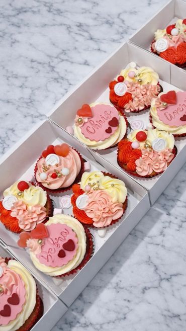 Valentine-themed cupcakes with personalized names and colorful decorations in white boxes.