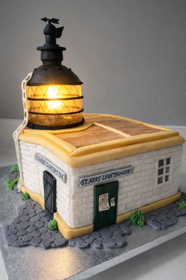 A detailed cake designed as St. Abbs Lighthouse with a glowing light.