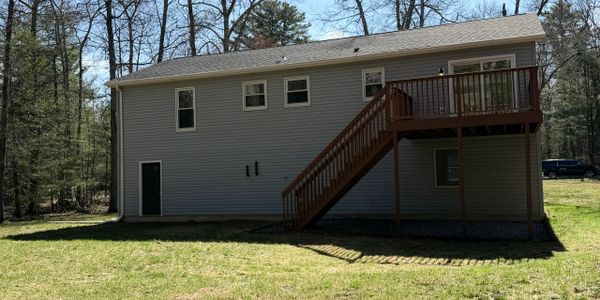 A two-story house with a wooden deck and stairs in a wooded area.