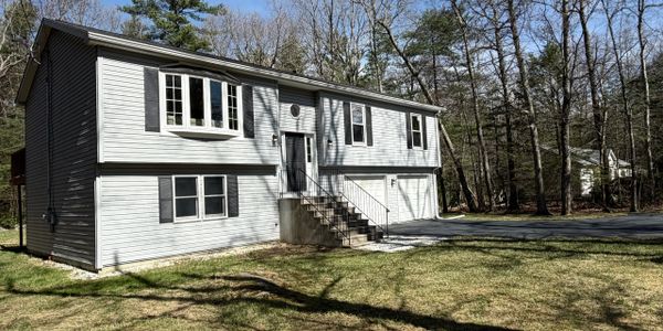 Gray two-story house with a front staircase and garage, surrounded by trees.
