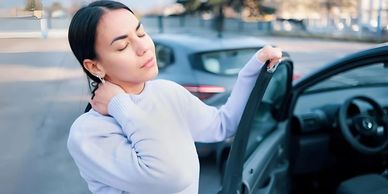 A woman experiencing neck pain while getting out of her car.