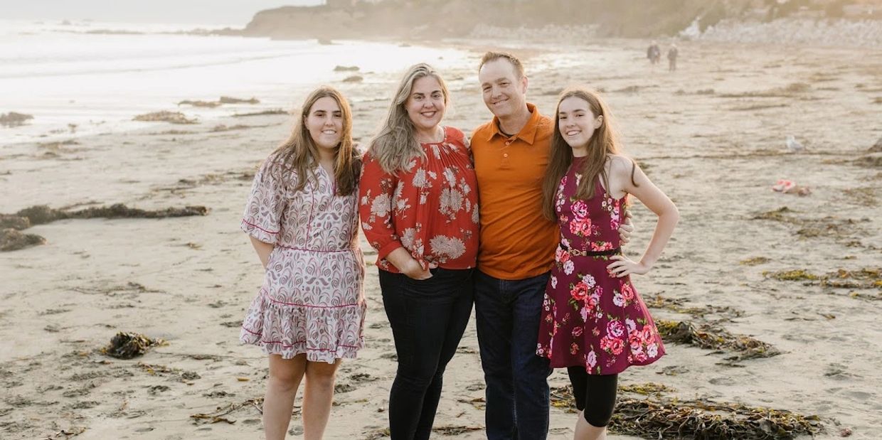 A family of four posing happily on a beach at sunset.