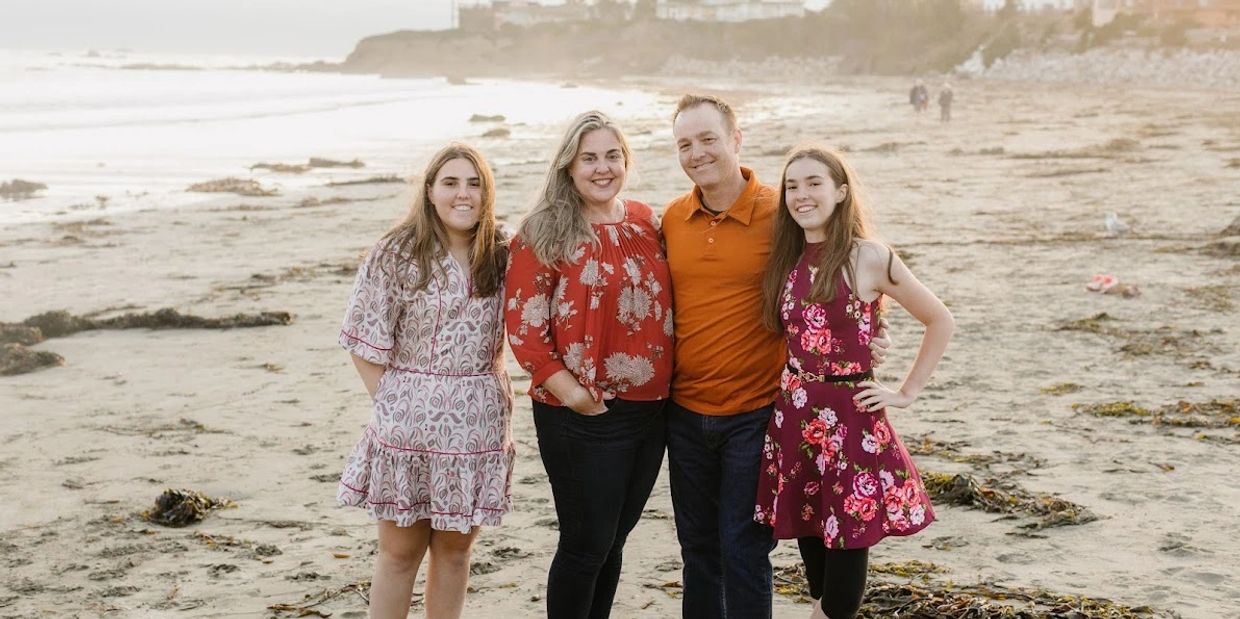 A smiling family of four posing on a beach at sunset.