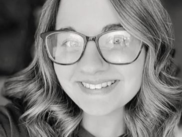 Smiling woman with glasses and wavy hair in black and white.