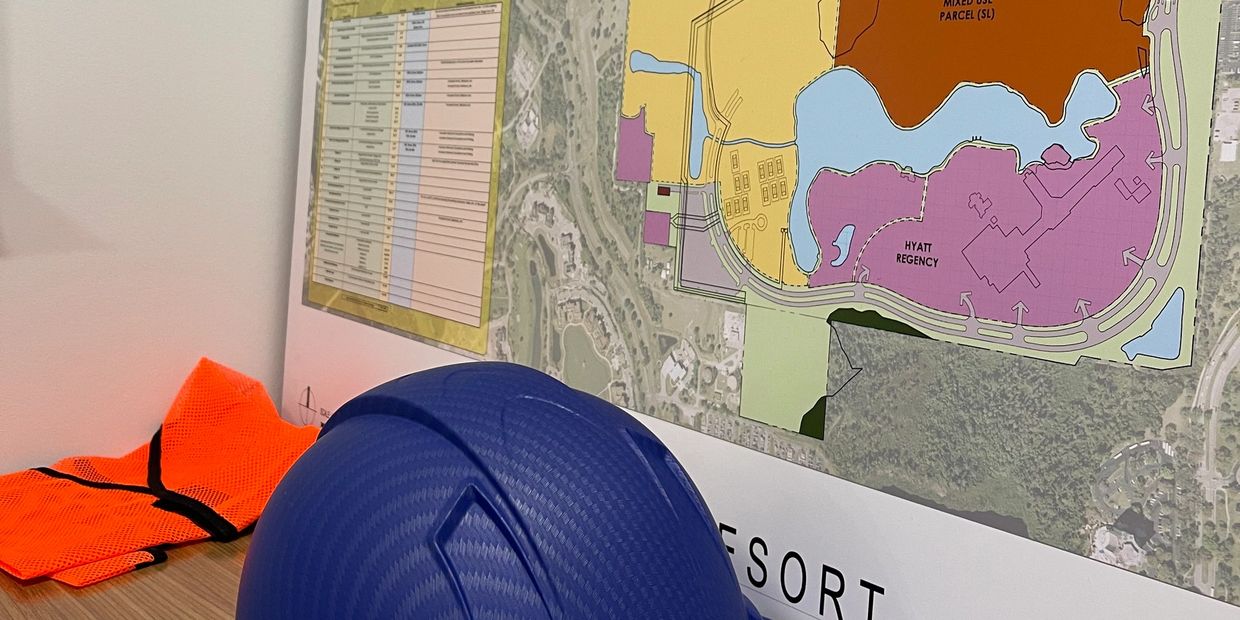 Blue hard hat and orange safety vest beside a resort development map.