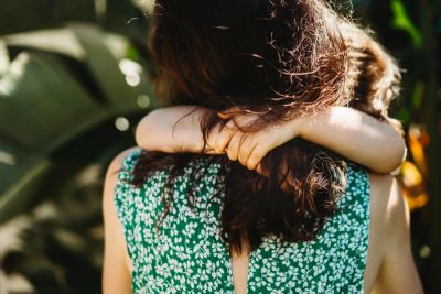Child hugging woman from behind outdoors.