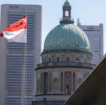 Singapore flag waving near a historic domed building with modern skyscrapers in the background.