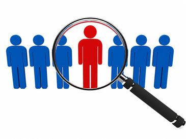 Magnifying glass highlighting a red figure among blue figures, symbolizing focus or selection.