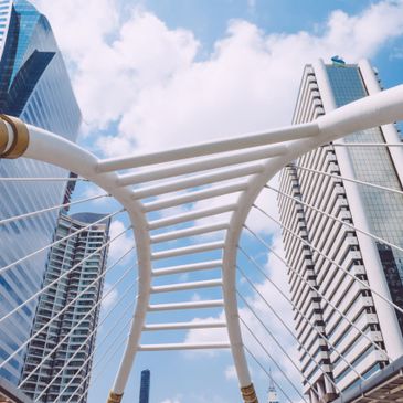 Modern urban bridge with people walking under a blue sky and tall buildings.