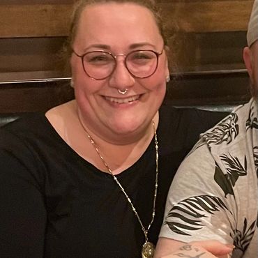 Smiling person with glasses and septum piercing.