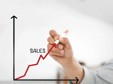 Hand drawing a rising sales graph with a red marker.