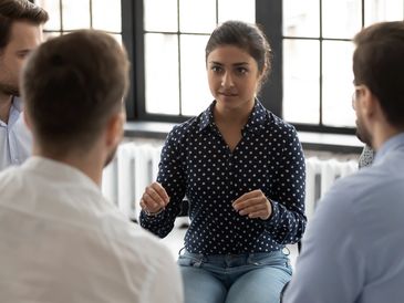 Woman leading a discussion with a group in a bright room.