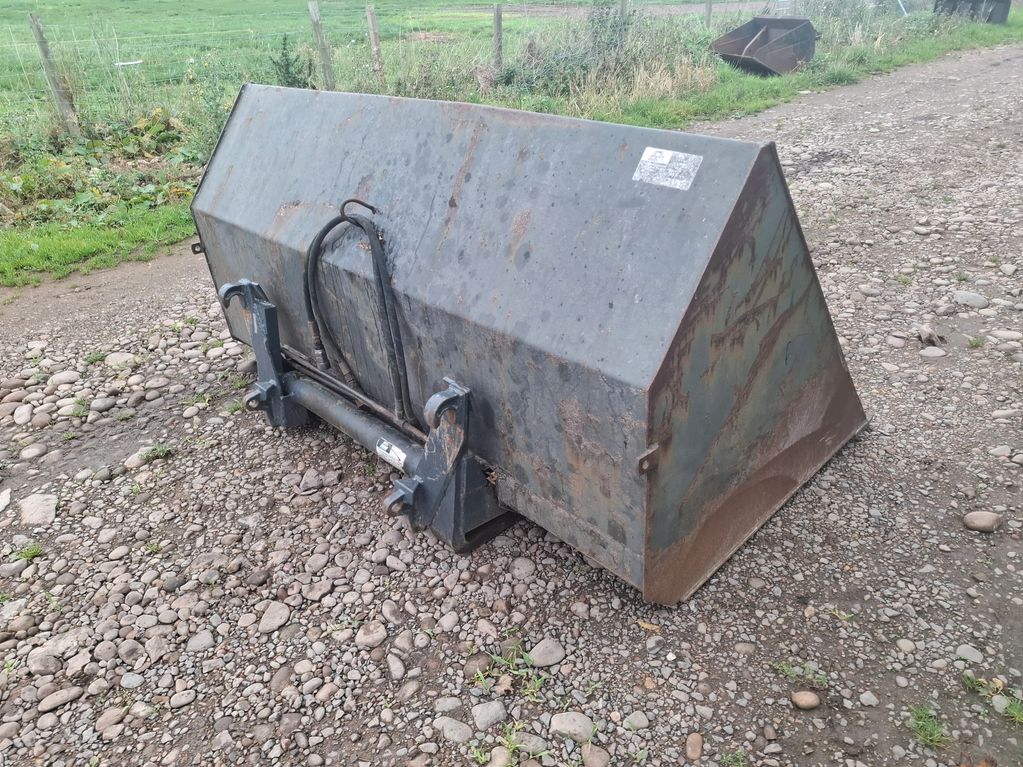 Large rusty metal bucket attachment for heavy machinery on a gravel path.