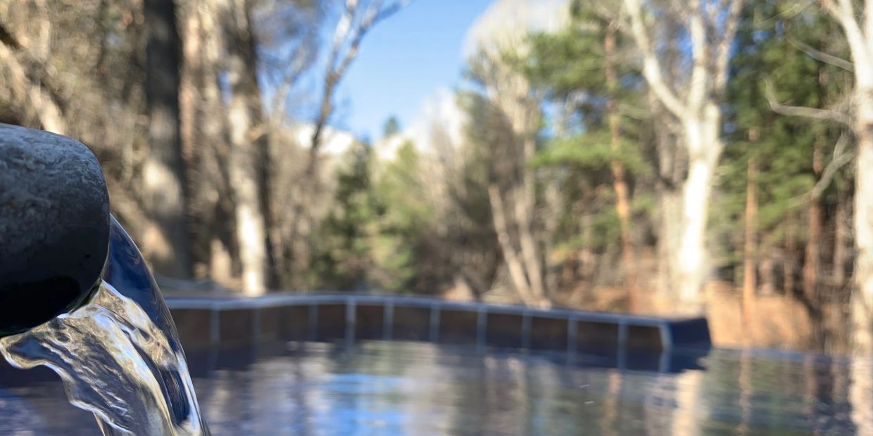 geothermal mineral water flowing out of pipe into the pool, trees in the background