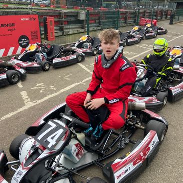 Young racer in red suit sitting on go-kart number 74 at a karting track.