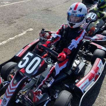 Go-kart racer in red and black gear ready to race, kart number 50.