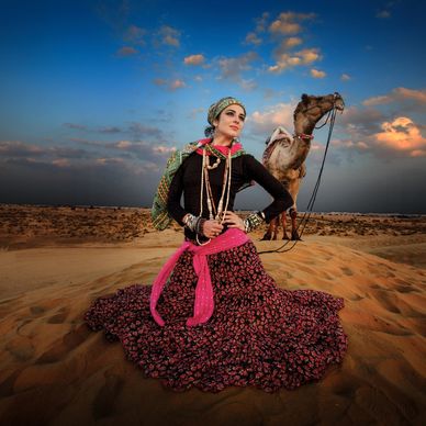 Woman in traditional attire posing with a camel in the desert.