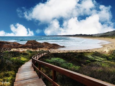 Wooden boardwalk leading to a sandy beach under a partly cloudy sky.