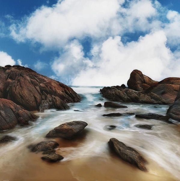 Rocky shoreline with smooth waves under a partly cloudy sky.