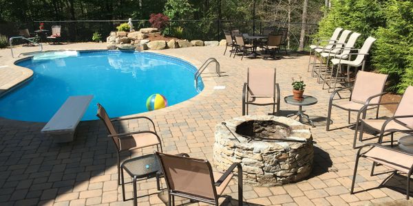 Sunny backyard with a pool, fire pit, and seating area on a stone patio.