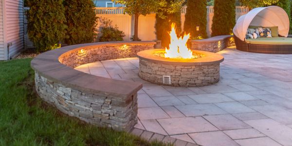 Stone fire pit with curved seating in a backyard patio at dusk.