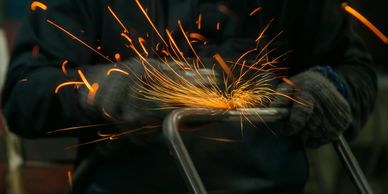 Sparks fly as a person grinds metal with protective gloves.
