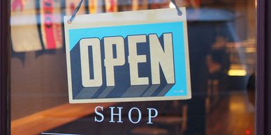 A blue and beige OPEN sign hanging on a shop window.
