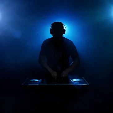 Silhouetted DJ mixing music in a dark, smoky environment with blue lighting.