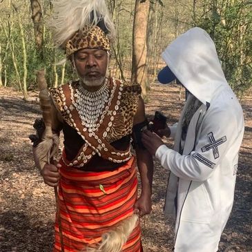A man in traditional African attire standing next to a person in a white hoodie.