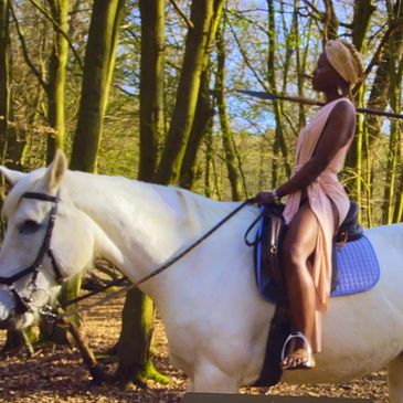 Woman in elegant pink dress riding a white horse in the forest.