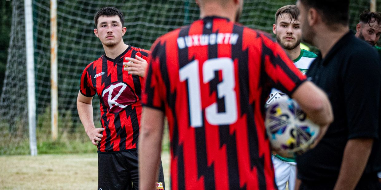 Soccer players in red and black jerseys during a match with a referee holding the ball.